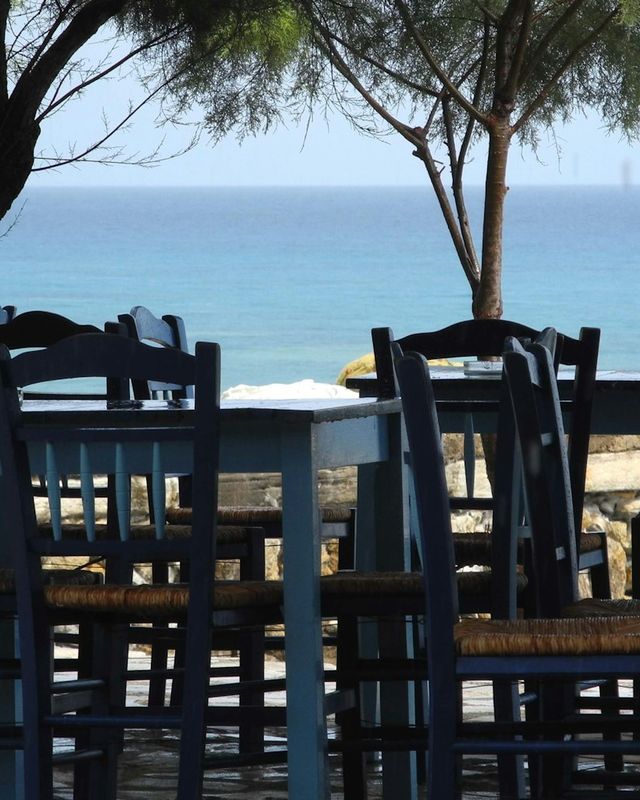 Τραπέζια ταβέρνας με μπλε καρέκλες δίπλα στη θάλασσα